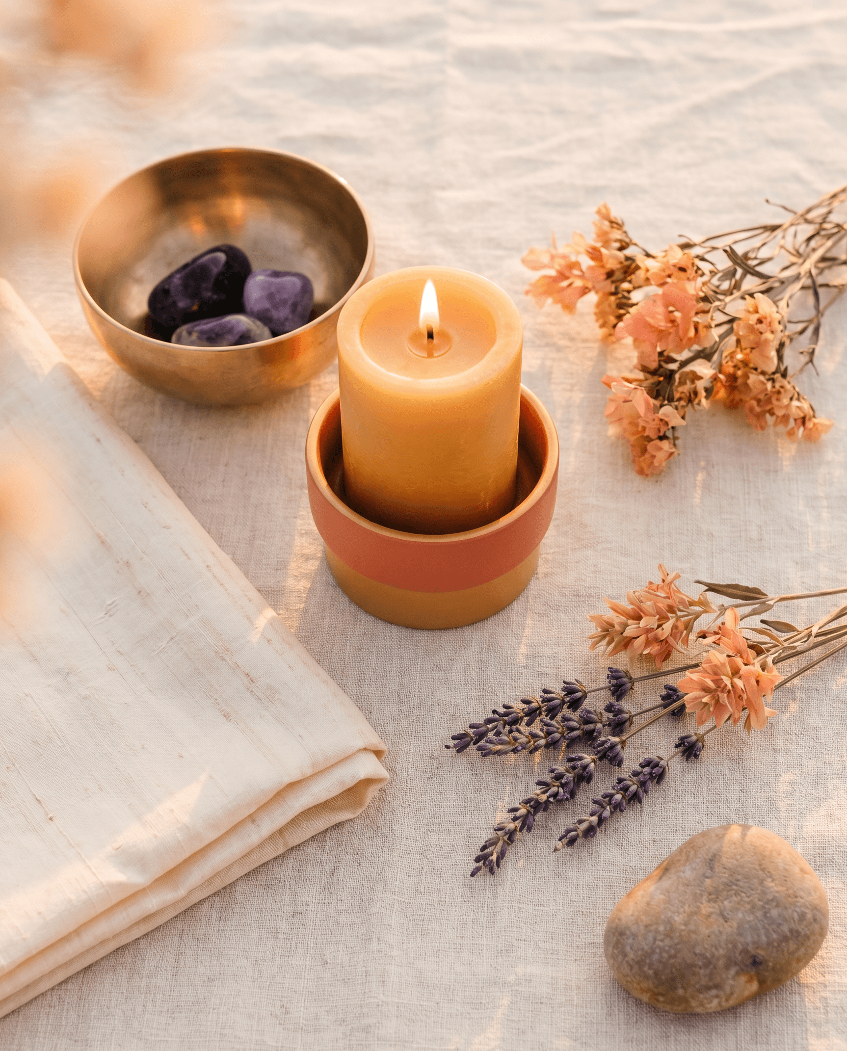 A single beeswax candle glowing on a prepared altar with a brass bowl and dried lavender